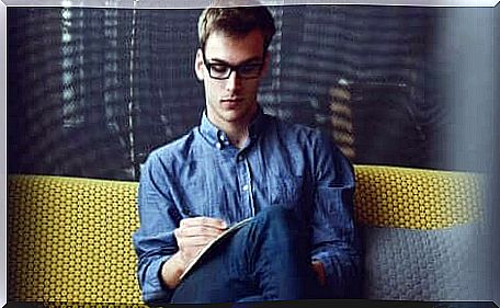 Boy with glasses reads sitting on the sofa.