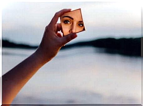 Woman holding a mirror in which her face is reflected.