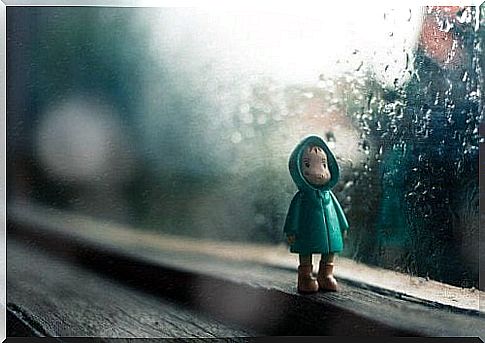 Baby doll in front of a window while it is raining outside